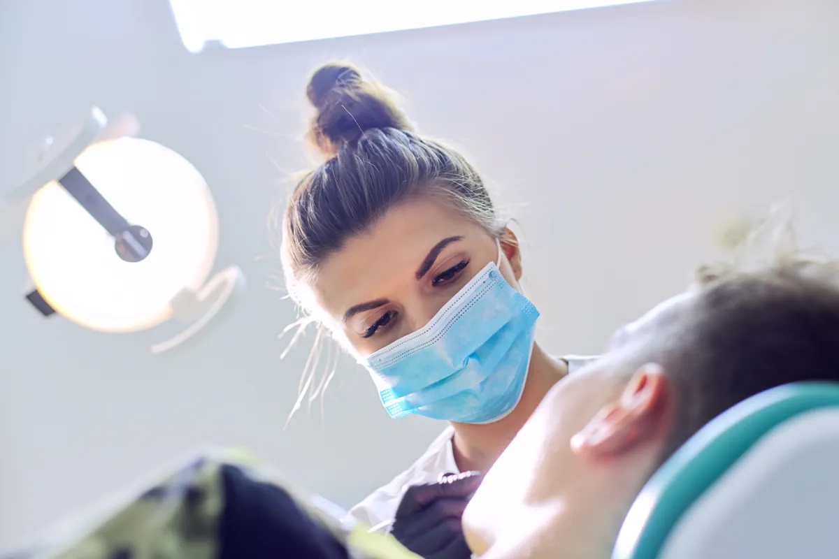 Masked dental professional treating a patient under an exam light
